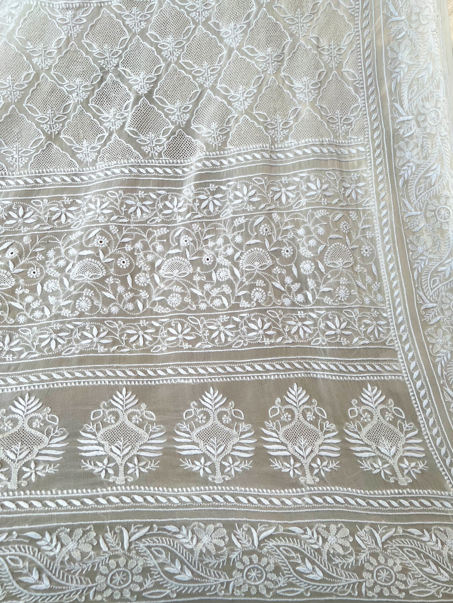 Intricate hand-embroidered Chikankari patterns on pearl white pure georgette fabric, showcasing elegant design.
