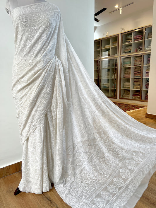 Elegant pearl white georgette saree featuring intricate Chikankari embroidery draped gracefully on a mannequin.