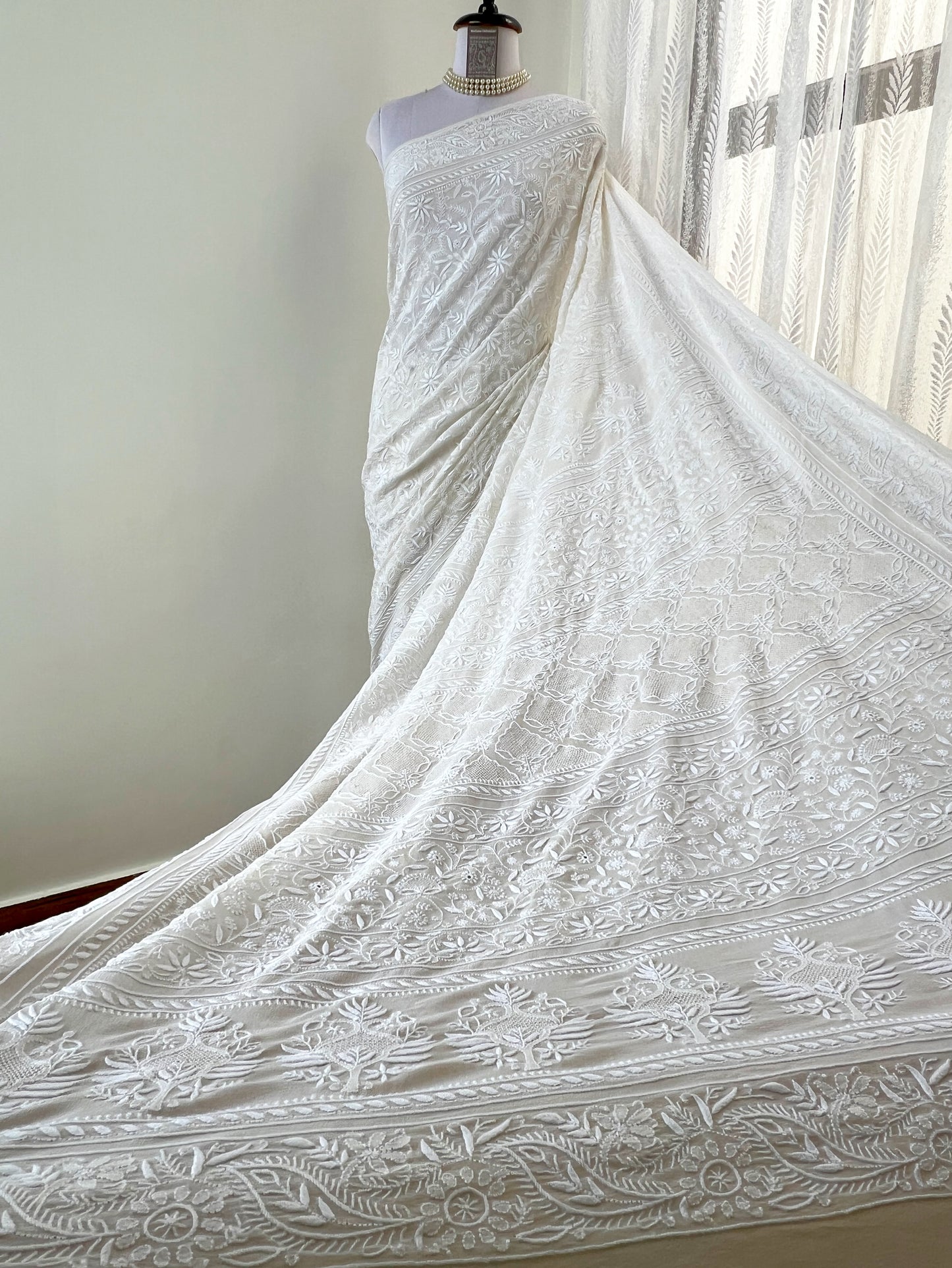 Elegant pearl white georgette saree featuring intricate chikankari embroidery and haath jaali work, flowing gracefully.