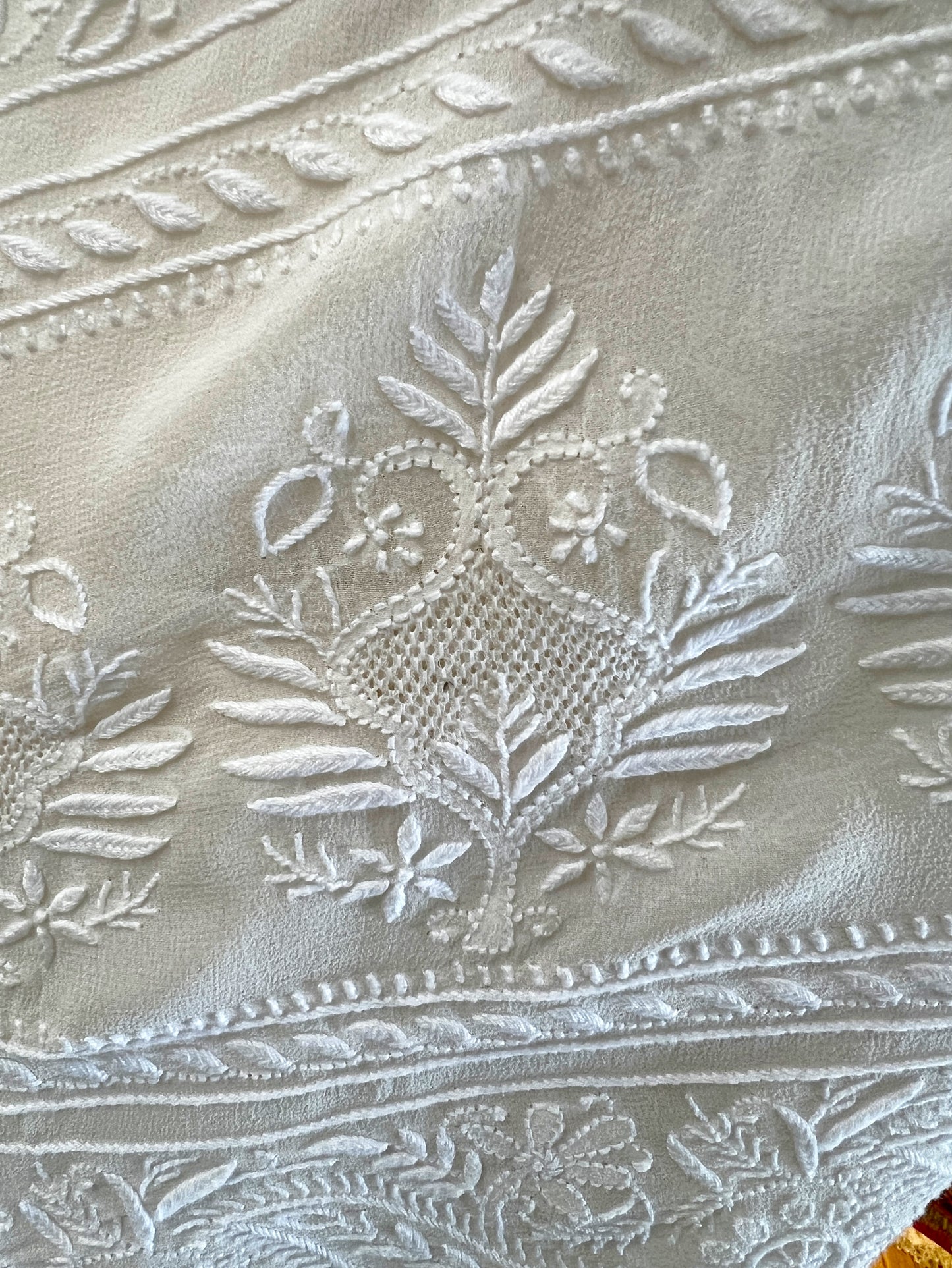 Intricate white Chikankari embroidery featuring floral and leaf patterns on pure georgette fabric.