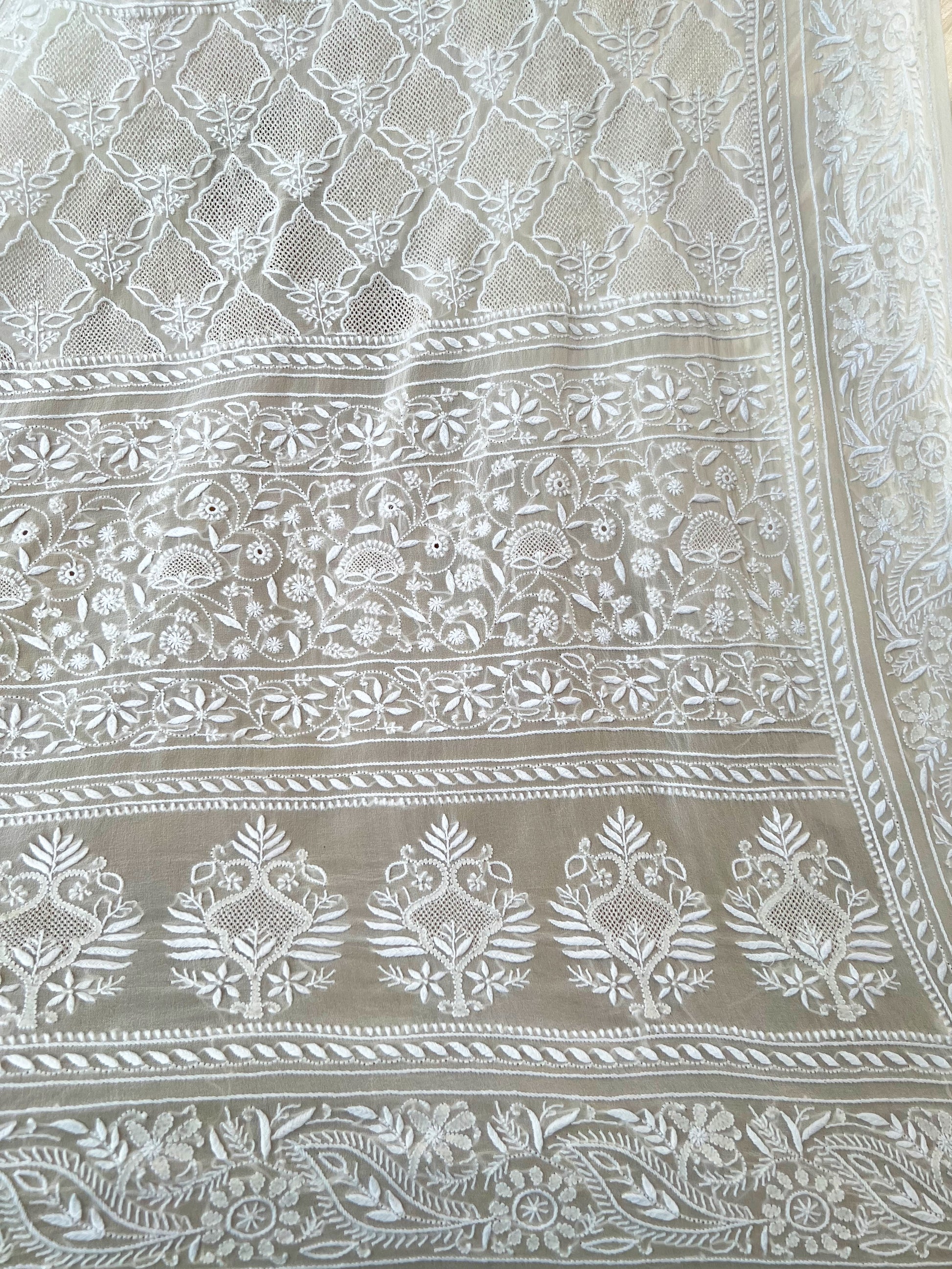Intricate hand-embroidered Chikankari patterns on pearl white pure georgette fabric, showcasing elegant design.