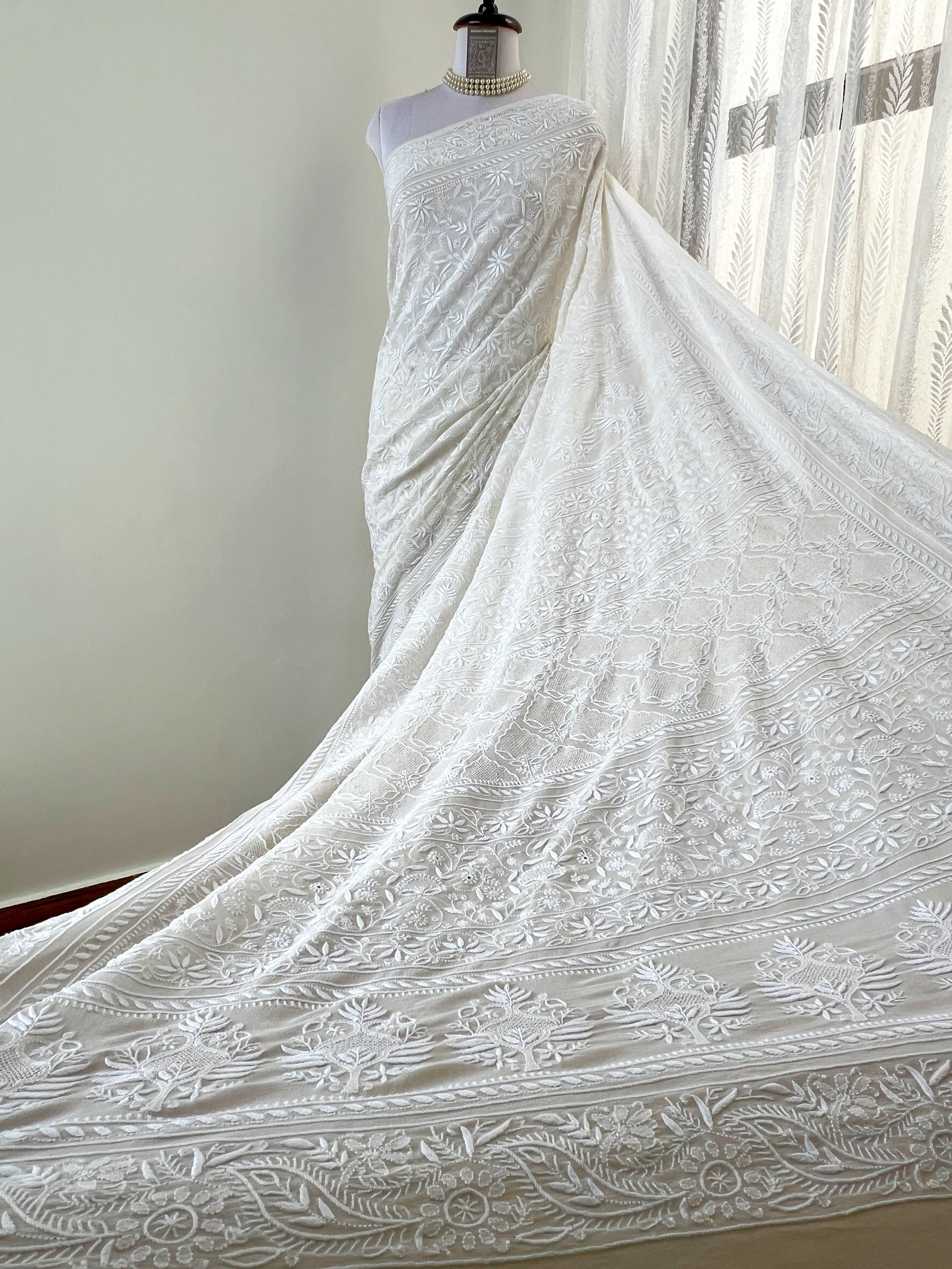 Elegant pearl white georgette saree featuring intricate chikankari embroidery and haath jaali work, flowing gracefully.