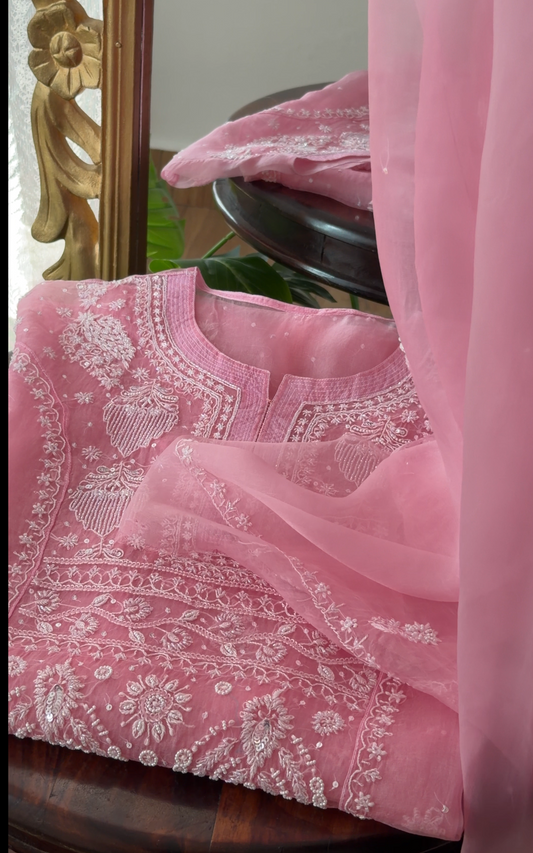 Pink Pure Organza Silk kurta set with Chikankari, delicate embroidery and embellishments on a wooden surface.